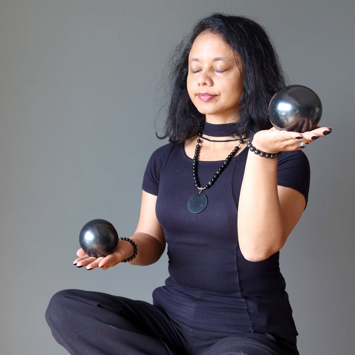 Woman holding two Shungite stones in each hand against a gray background