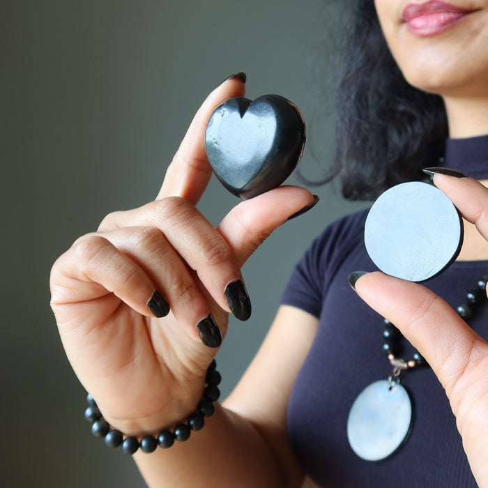 Person holding two black Shungite  stone heart-shaped pendants against a neutral background