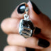  Elite Shungite pendant held by a hand with black nail polish against a dark background
