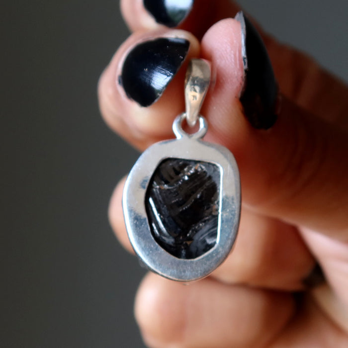 Silver pendant with a black Elite Shungite stone held by a hand with black nail polish.