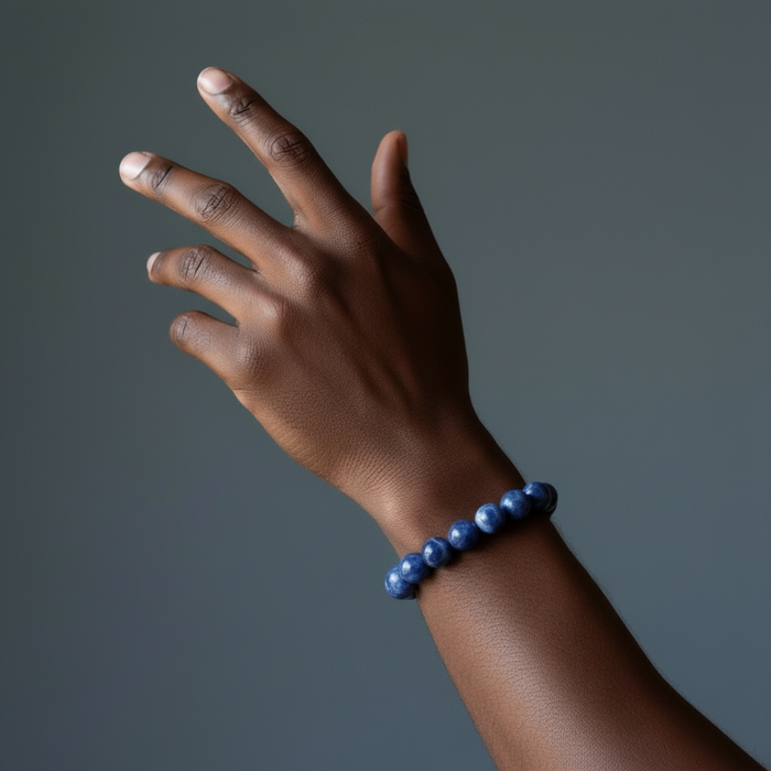 Hand wearing a blue sodalite beaded bracelet on a gray background