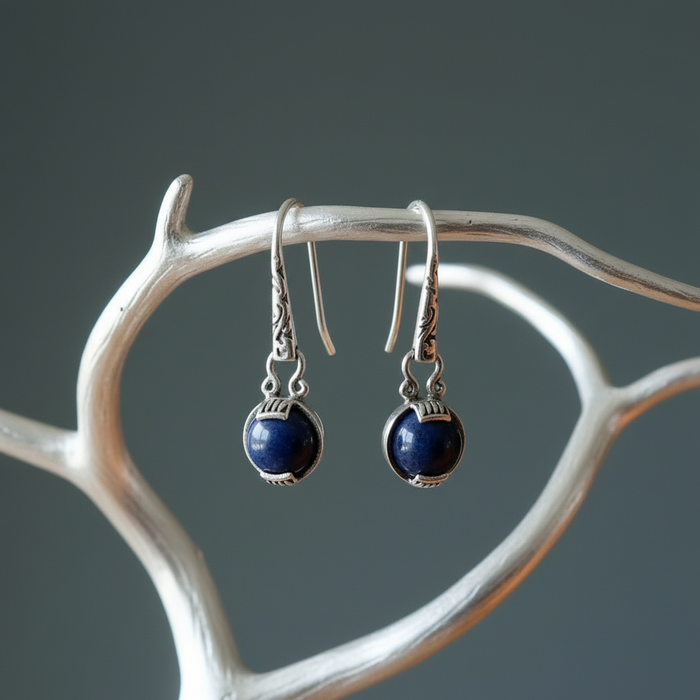 Pair of silver earrings with blue sodalite stones on a branch against a gray background