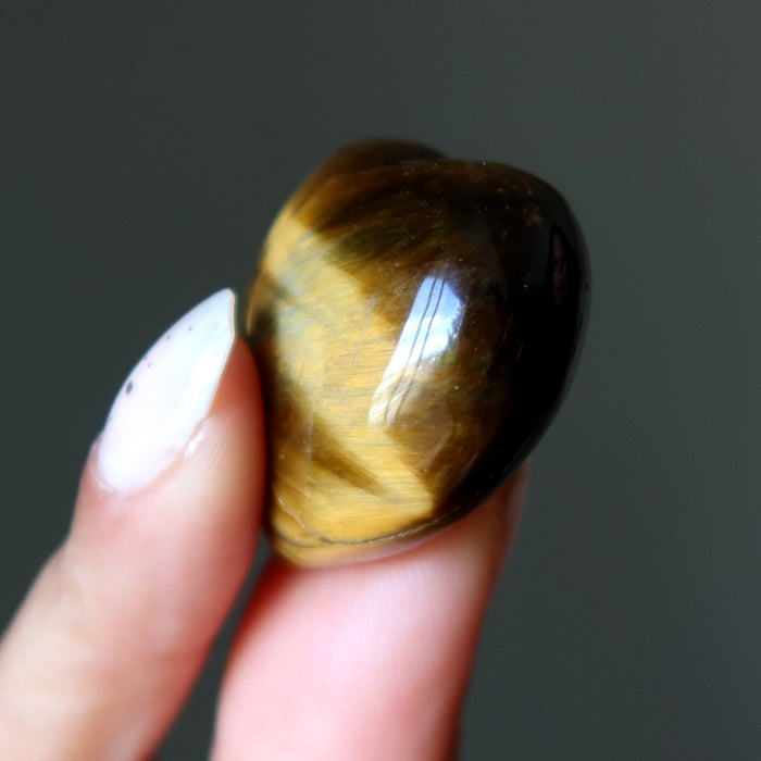 Hand holding a tiger's eye stone against a dark background