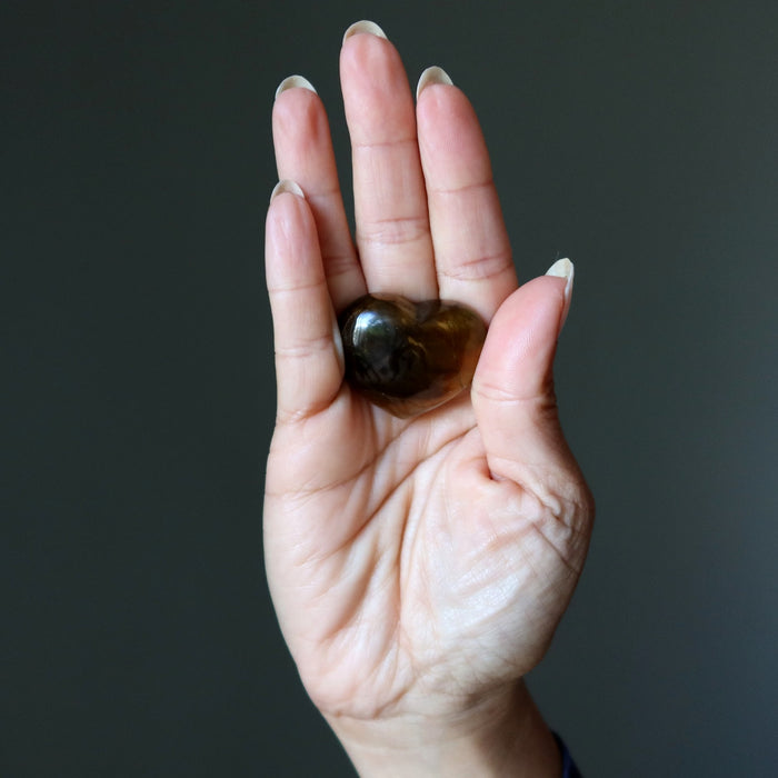 Hand holding a small tigers eye heart against a dark background