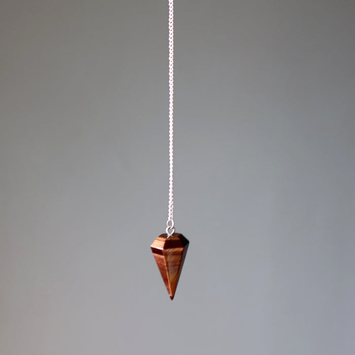  tigers eye pendulum on a chain against a gray background
