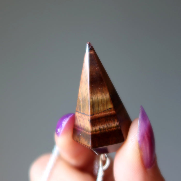 Tiger's eye crystal held by a hand with purple nail polish against a gray background