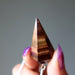 Tiger's eye crystal held by a hand with purple nail polish against a gray background