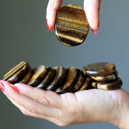 Hand holding a stack of tiger eye stones against a gray background