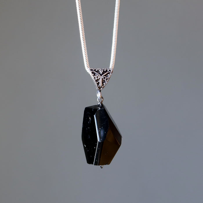 Black tourmaline pendant on a silver chain against a gray background