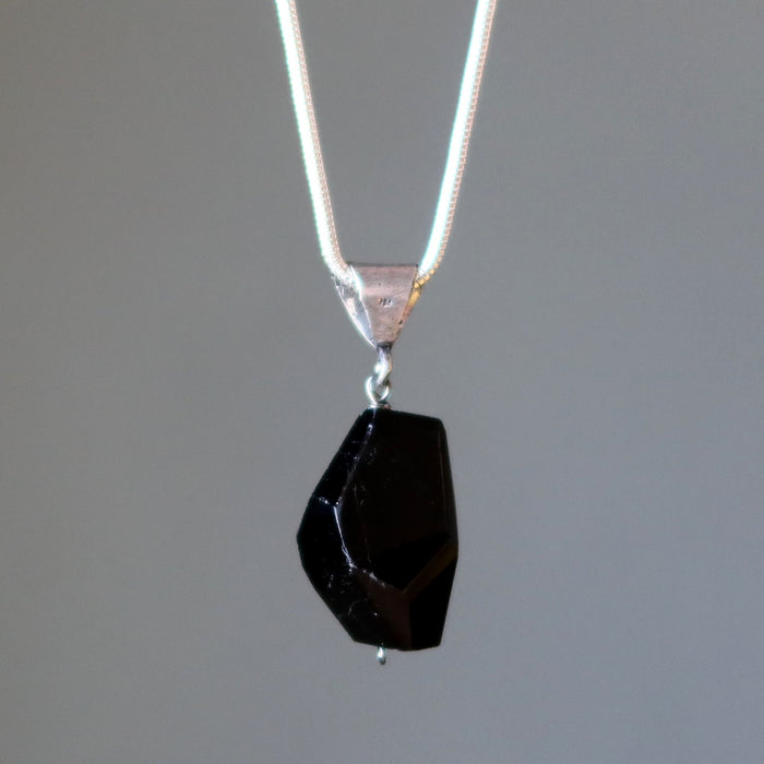 Black tourmaline stone pendant on a silver chain against a gray background