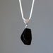 Black tourmaline stone pendant on a silver chain against a gray background