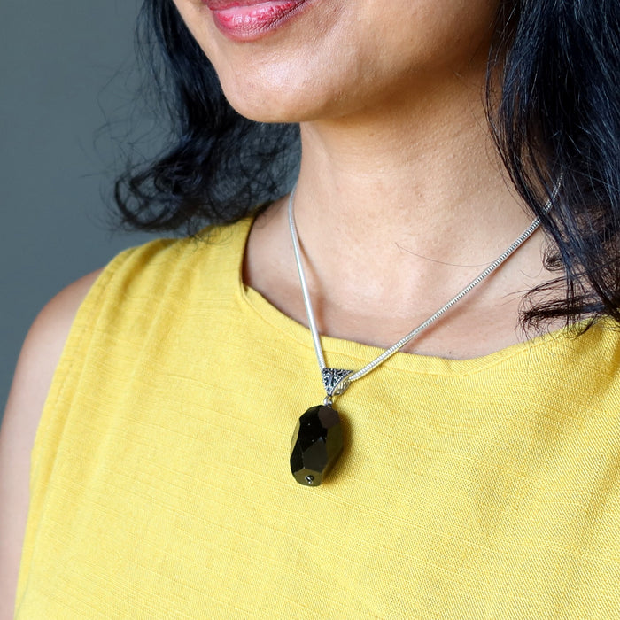 Woman wearing a yellow top and a necklace with a black tourmaline pendant against a gray background
