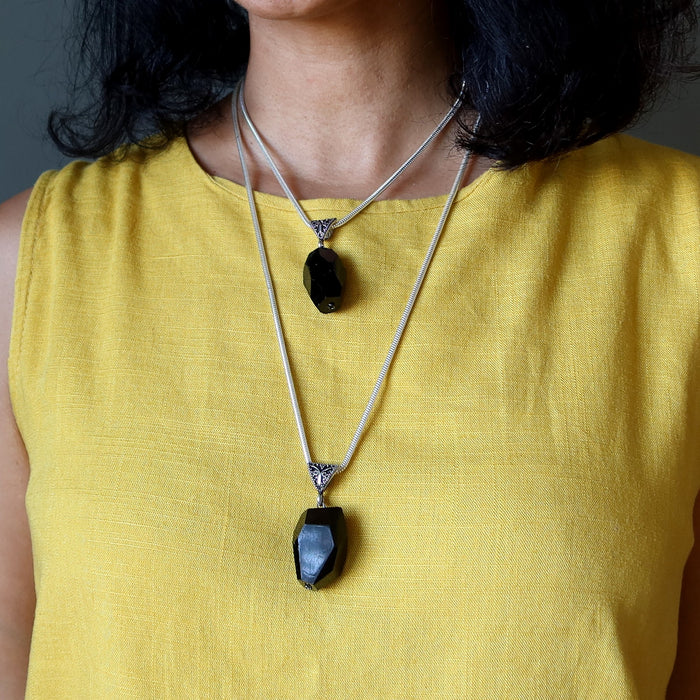 Person wearing a yellow top with two black tourmaline pendant necklaces.