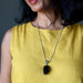 Woman wearing a yellow top and a necklace with a black tourmaline pendant against a dark background
