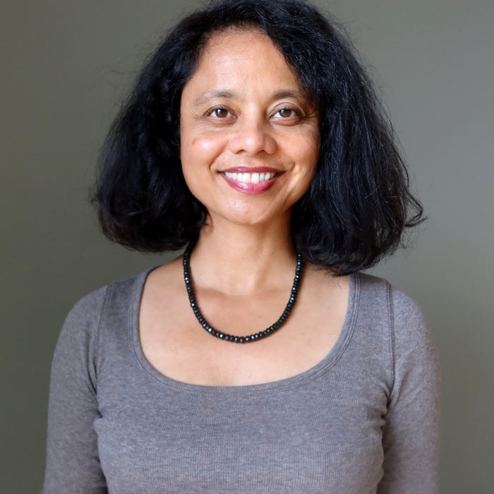 Woman with short black hair wearing a gray shirt and black Tourmaline necklace against a plain background