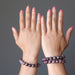 Two hands wearing red tourmaline beaded bracelets on a gray background