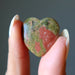 Heart-shaped multicolored unakite stone held between fingers against a neutral background