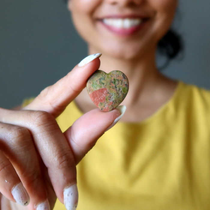 Person holding a unakite heart-shaped stone with a blurred background