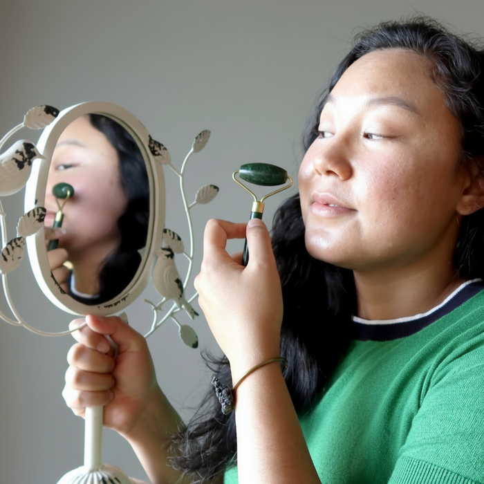 Woman using a jade roller in front of a mirror