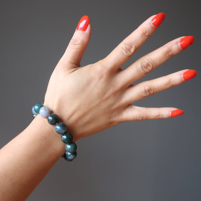 hand wearing green and white moss agate round beaded stretch bracelet