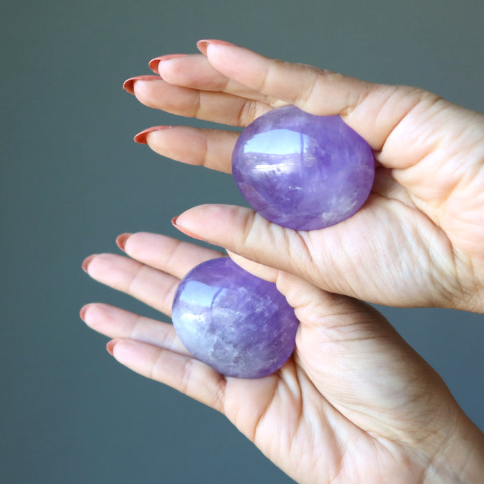 palms holding pair of purple amethyst polished ovalish palm stones