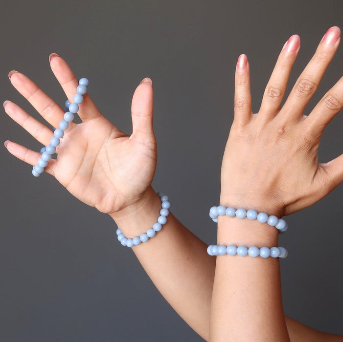 two hands wearing blue angelite round beaded stretch bracelets