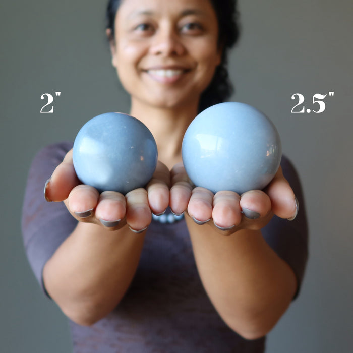 sheila of satin crystals holding out a 2" and a 2.5" angelite sphere