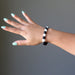 woman's hand wearing blue aquamarine and black rainbow obsidian stretch bracelet
