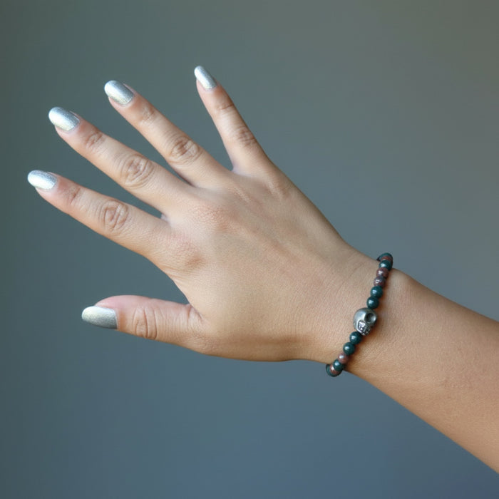 female hand wearing pyrite skull and round bloodstone beaded stretch bracelet