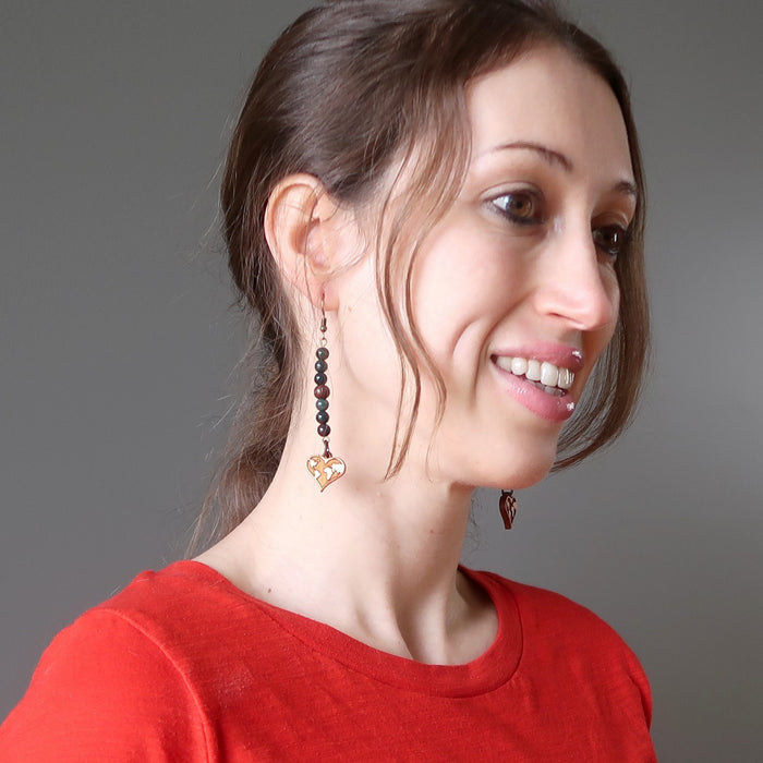 female model wearing brown wood heart shaped world map charms on dark green bloodstone beaded earrings and antiqued steel earwire