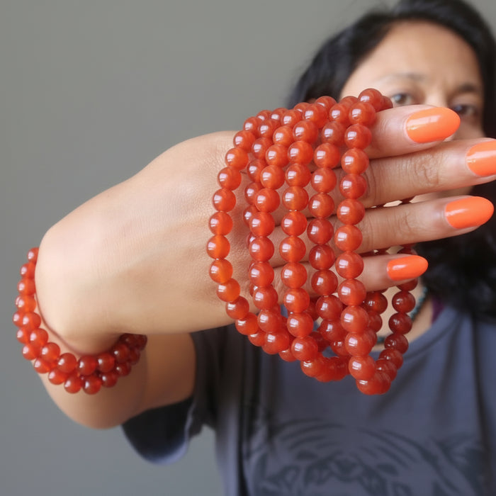 sheila of satin crystals holding a stack of carnelian bracelets