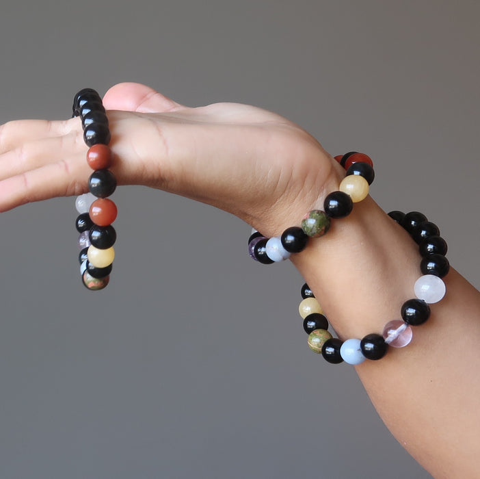 hand holding and wearing 3 rainbow obsidian and natural chakra stone stretch bracelets