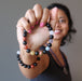 sheila of satin crystals holding out a rainbow obsidian and natural chakra stone stretch bracelet beaded with round gemstones