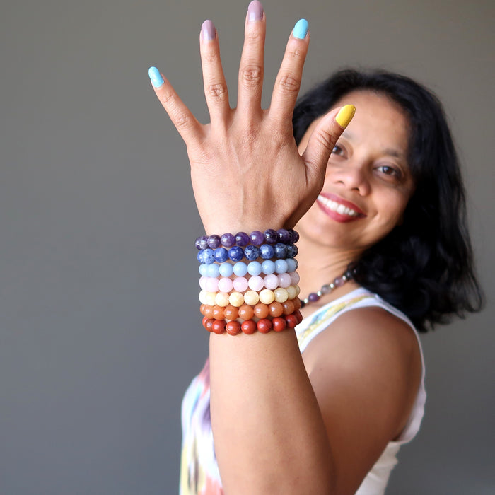 sheila of satin crystals wearing set of 7 chakra bracelets with amethyst, sodalite, angelite, rose quartz, calcite, aventurine and red jasper holding a tibetan singing bowl