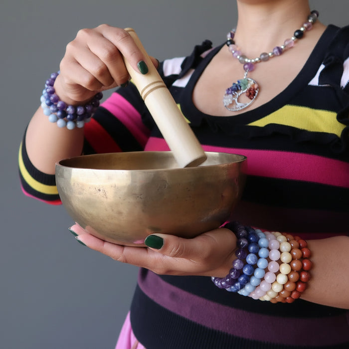 sheila of satin crystals wearing set of 7 chakra bracelets with amethyst, sodalite, angelite, rose quartz, calcite, aventurine and red jasper holding a tibetan singing bowl
