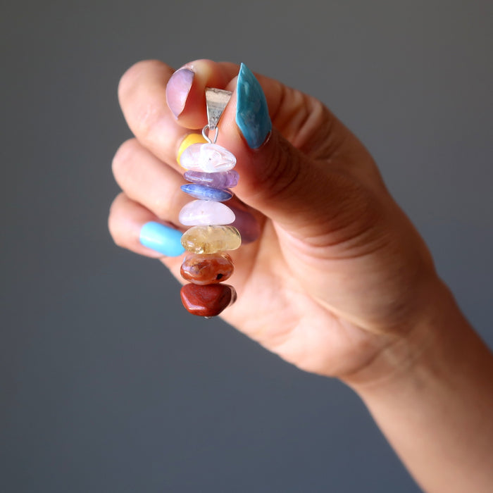 hand holding a stacked gemstone chakra pendant 