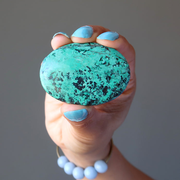 hand holding blue-green and black chrysocolla oval cabochon