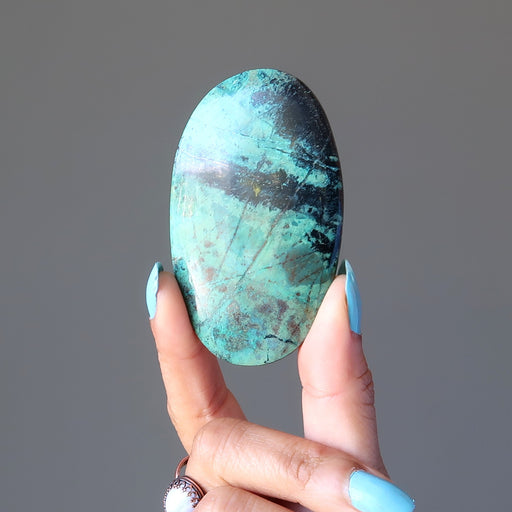 hand holding blue-green and black chrysocolla oval cabochon