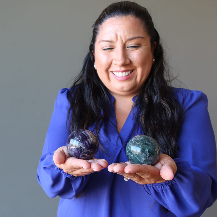 model holding green purple rainbow Fluorite Spheres one on each hand