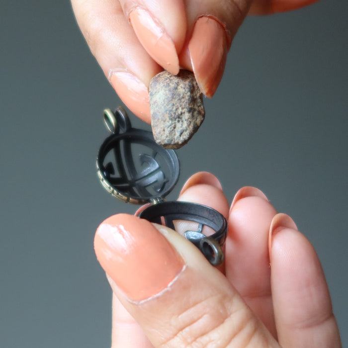 hand putting gao-guenie meteorite in locket pendant