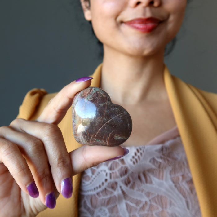 hand holding green and red garnet heart over heart chakra