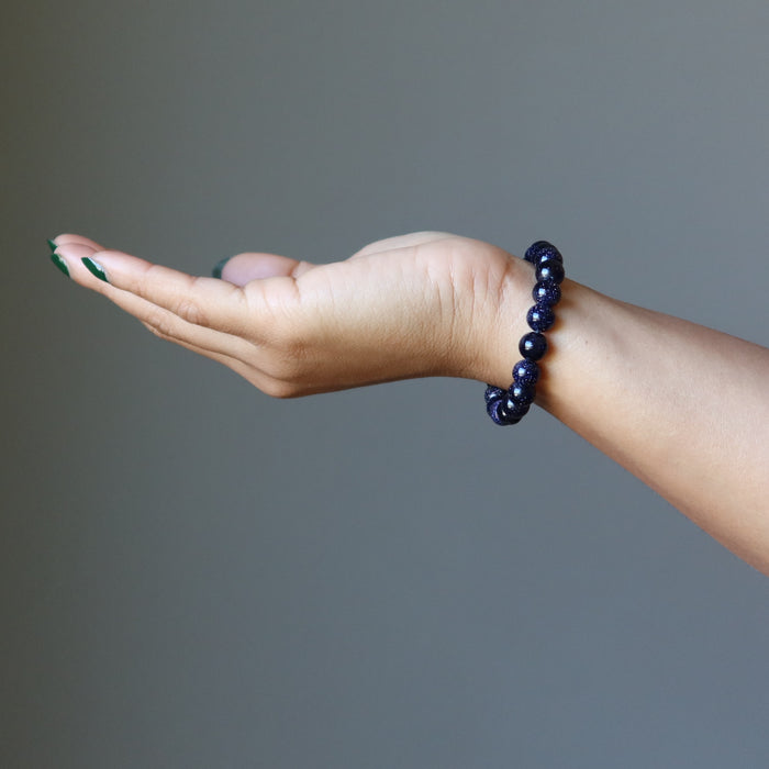 female hand wearing blue goldstone bracelet