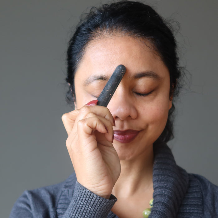 sheila of satin crystals holding a hematite massage wand to her third eye chakra