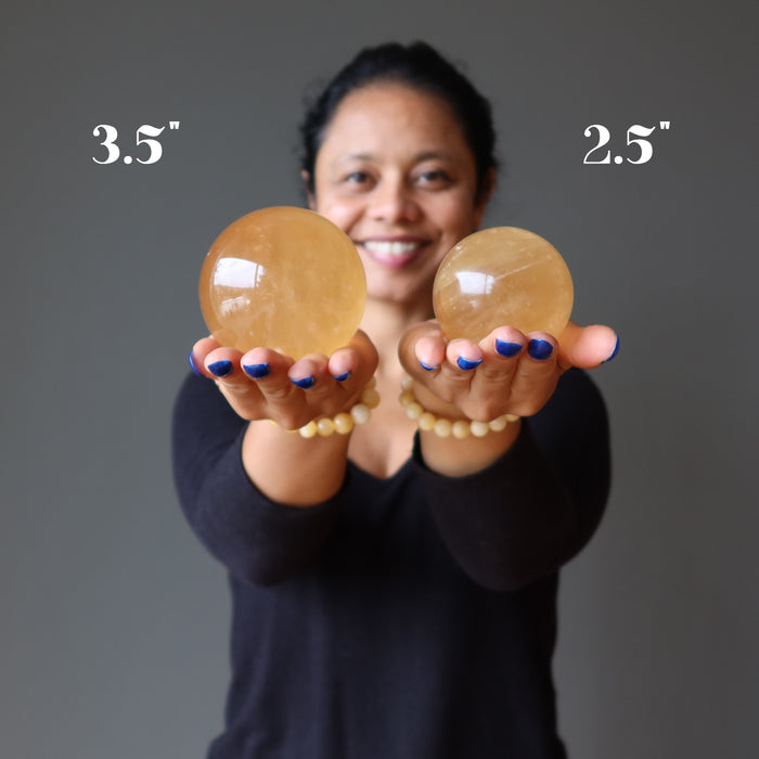 sheila of satin crystals holding out 2 golden calcite sphere to show size difference