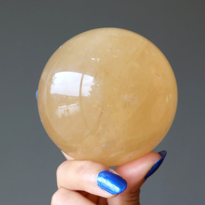 hand holding a honey calcite sphere