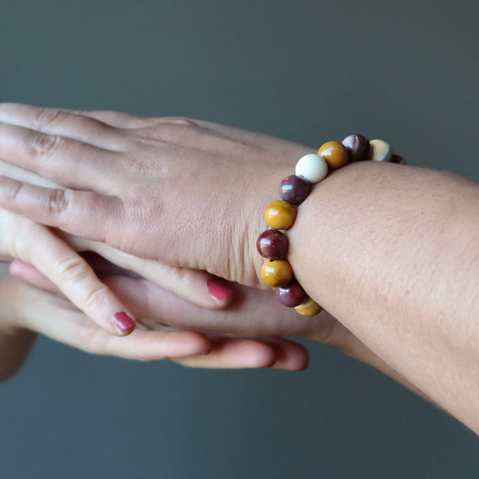 stacked hands wearing multi colored mookaite jasper round beaded stretch bracelet