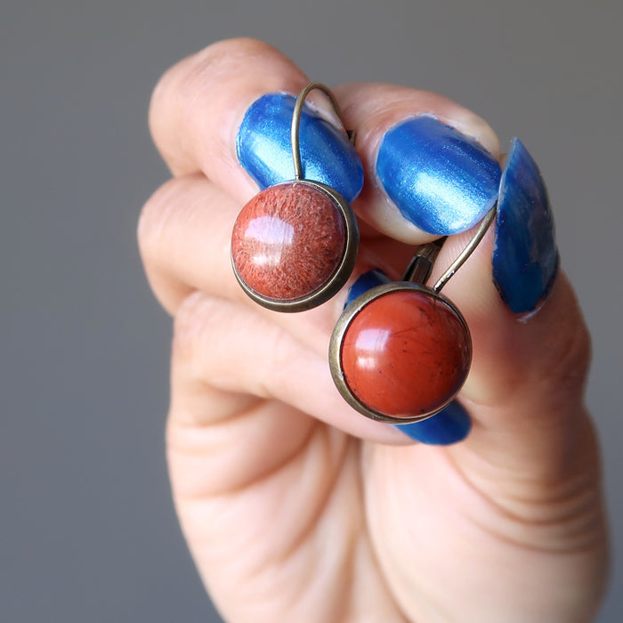 hand holding a red jasper in antique bronze leverback earrings
