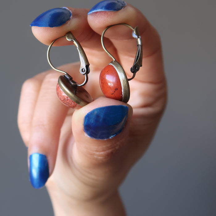 hand holding a red jasper in antique bronze leverback earrings