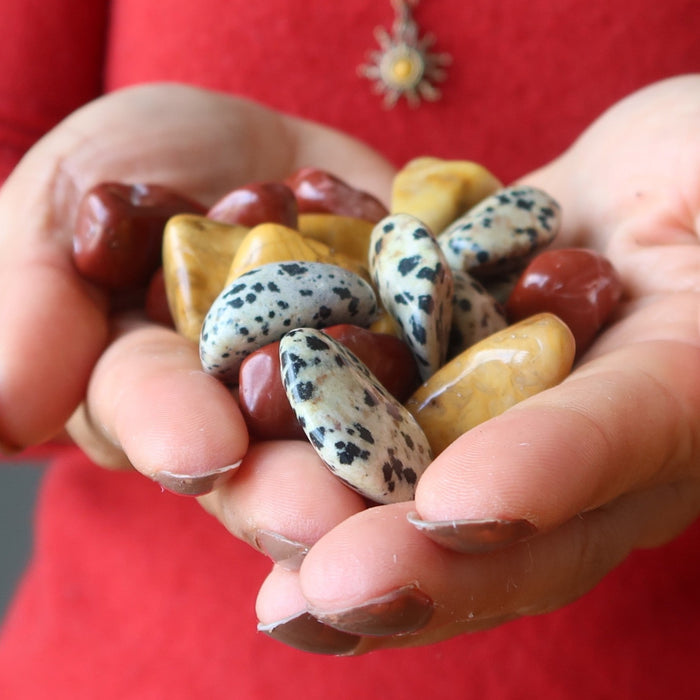 hands holding yellow, red, and dalmatian jasper tumbled stones