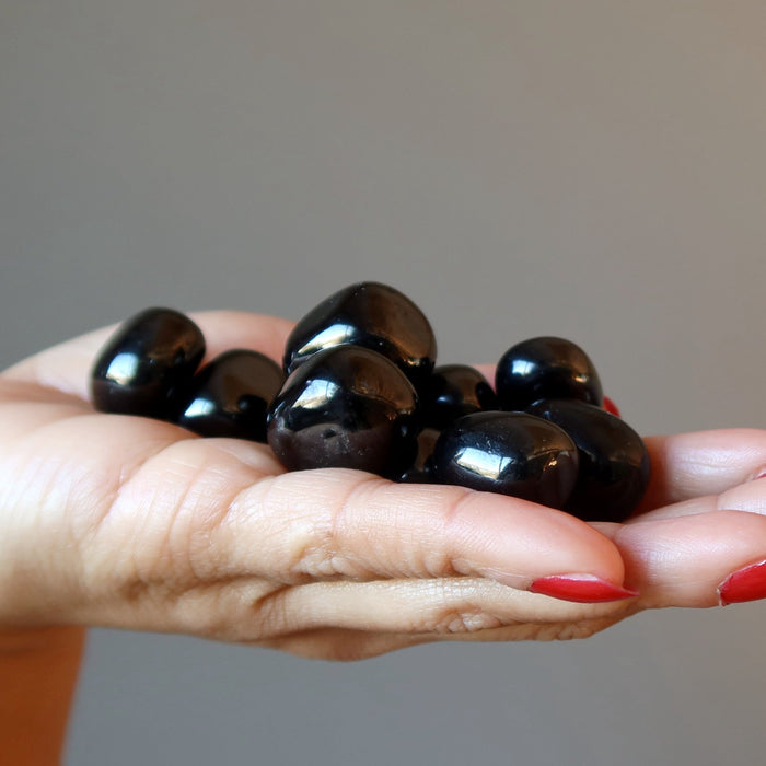 hand holding a pile of jet tumbled stones